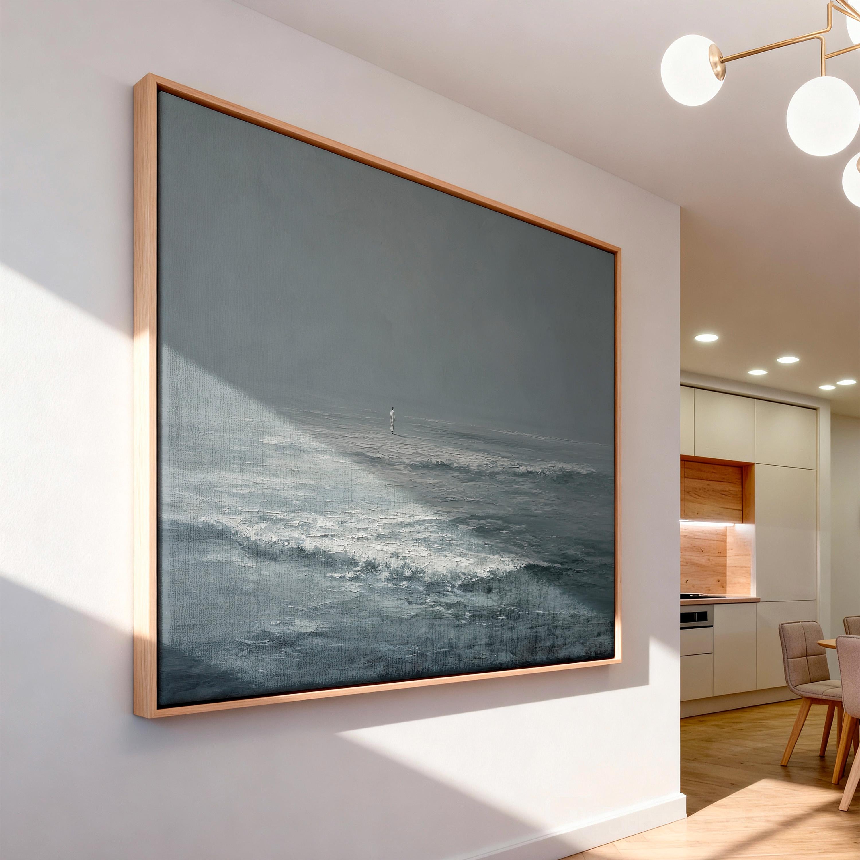 May include: A large, framed canvas painting depicting a seascape in shades of gray and white. The artwork features a lone figure on the horizon, with waves crashing in the foreground. The frame is made of light-colored wood, adding a natural touch.